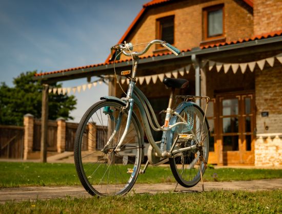 Noskaņu fotoattēls, kas raksturo brīvdienu māju Grāvendāles pienotava. Priek&scaron;plānā ir velosipēds, kas raksturo aktīvo atpūtu laukos, bet fonā ir redzama ēka un izkarināti vimpeļi, kas pie&scaron;ķir svētku noskaņu.