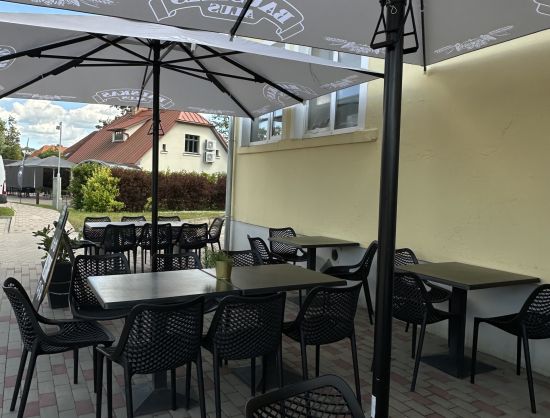 Kafejnīcas 'Grāfs' āra terase vasaras sezonā: galdiņi ar saulessargiem un ērtiem krēsliem, blakus autostāvvietai.