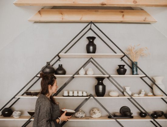 Keramikas izstrādājumi gaumīgi izkārtotā dekoratīvos piramīdas veida sienas plauktos. Mūsdienīga amatniecība Latvijā: 'Laima Ceramics' darbnīca un suvenīru veikals. Dizaina keramikas trauki, meistarklases un ekskursijas rado&scaron;iem ceļotājiem Bauskas apkārtnē.