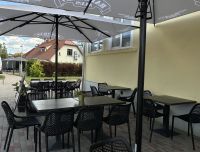 Kafejnīcas 'Grāfs' āra terase vasaras sezonā: galdiņi ar saulessargiem un ērtiem krēsliem, blakus autostāvvietai.