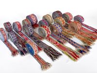 Krāsainas ar rokām austas latvie&scaron;u tradicionālās jostas ar ģeometriskiem rakstiem un bārkstīm, izkārtotas rindā uz balta fona.