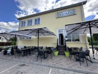 Kafejnīcas 'Grāfs' āra terase vasaras sezonā: galdiņi ar saulessargiem un ērtiem krēsliem, ko ieskauj Rundāles pils vēsturiskā vide un sakoptā apkārtne.