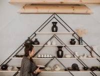 Keramikas izstrādājumi gaumīgi izkārtotā dekoratīvos piramīdas veida sienas plauktos. Mūsdienīga amatniecība Latvijā: 'Laima Ceramics' darbnīca un suvenīru veikals. Dizaina keramikas trauki, meistarklases un ekskursijas rado&scaron;iem ceļotājiem Bauskas apkārtnē.